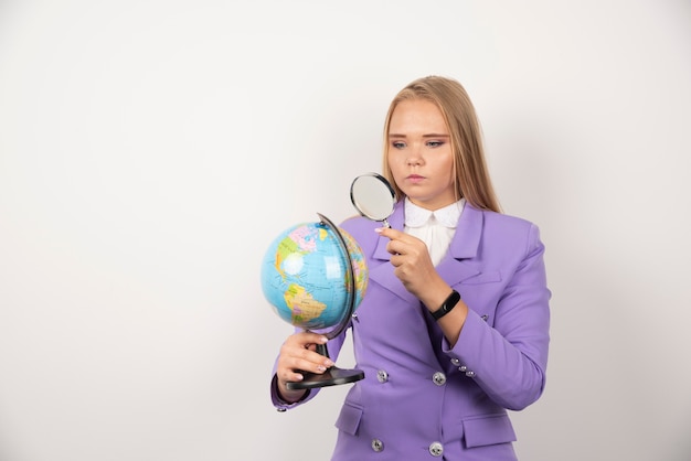 Professeur de femme regardant le globe avec une loupe avec une expression sérieuse.