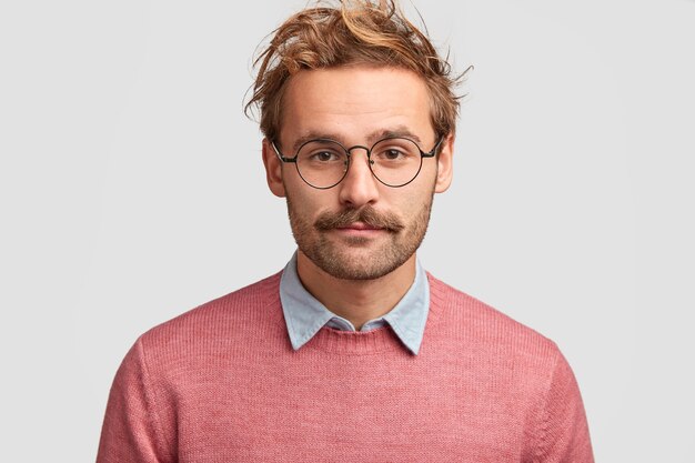 Professeur d'homme sérieux avec un regard intelligent et confiant, a une barbe et une moustache, écoute la réponse de l'élève, porte un pull rose, des lunettes rondes
