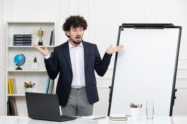 Professeur instructeur brune avec ordinateur en costume et tableau blanc en classe choqué en agitant les mains