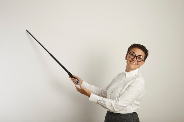 Professeur de race blanche habillée de façon conservatrice dans des verres ronds laids tenant un pointeur vers un tableau blanc vide et souriant désagréablement