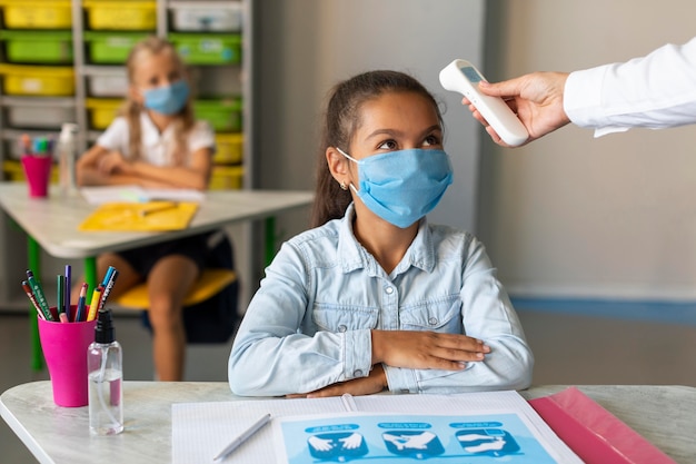 Professeur de vue de face prenant la température d'un élève