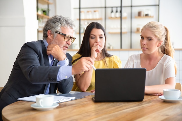 Professionnel mature expliquant les détails du projet aux jeunes clients, pointant sur l'affichage du PC