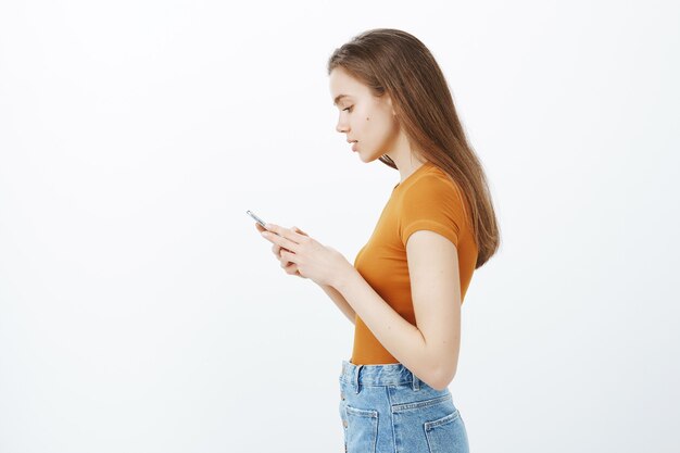 Profil de la belle jeune femme utilisant un téléphone mobile, faire du shopping dans l'application, envoyer des messages ou modifier des photos