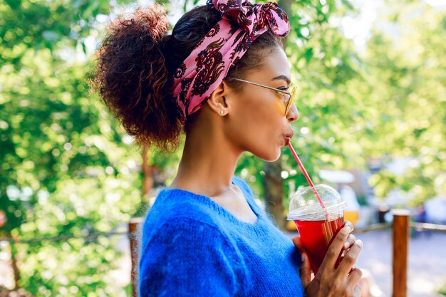 Profil de femme noire heureuse avec bandeau élégant à l'horizon et tenant la limonade cerise sur les mains.