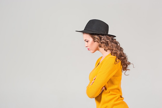 Le profil de la fille émotionnelle au chapeau sur le mur gris du studio