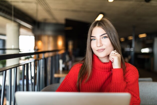 Profiter des avantages du Wi-Fi gratuit. Belle jeune femme au chapeau funky travaillant sur ordinateur portable et souriant tout en étant assis à l'extérieur