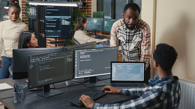 Photo gratuite programmeur assis au bureau avec plusieurs écrans exécutant du code parlant avec un collègue de l'algorithme d'intelligence artificielle. développeurs de logiciels réalisant un projet innovant d'intelligence artificielle.