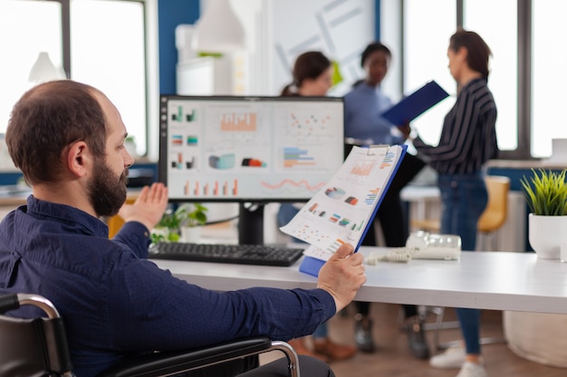 Photo gratuite projet de directeur marketing handicapé assis en fauteuil roulant dans un bureau de démarrage lisant des rapports de vérification