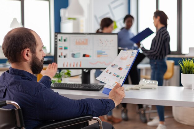 Projet de directeur marketing handicapé assis en fauteuil roulant dans un bureau de démarrage lisant des rapports de vérification