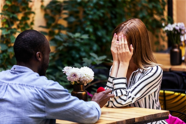 Photo gratuite proposition d'un garçon africain à une fille de race blanche à la terrasse d'un restaurant en plein air confortable