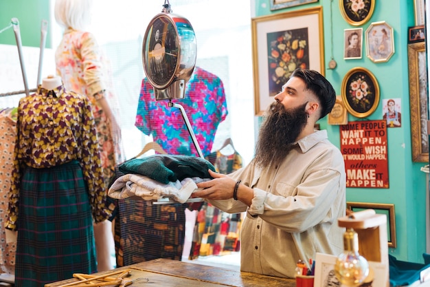 Propriétaire barbu vérifiant le poids du tissu sur des balances dans son magasin de vêtements