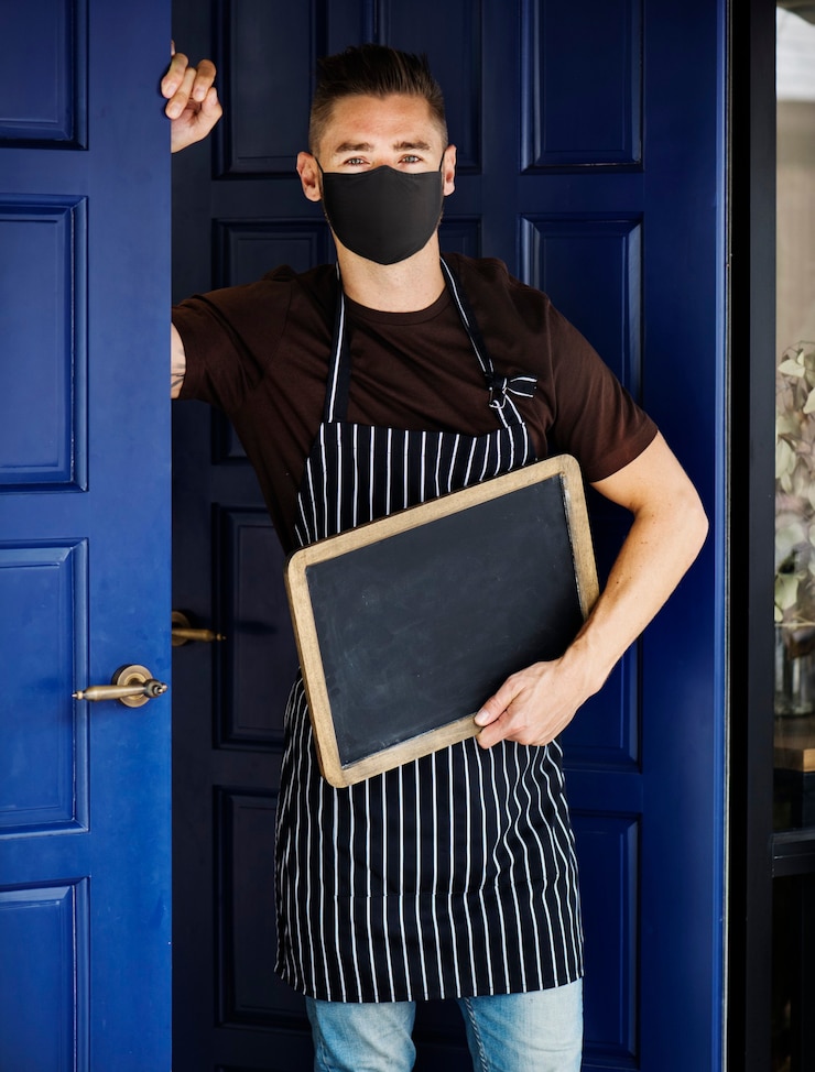 Photo gratuit propriétaire de la boutique en masque à l'extérieur du café dans la nouvelle normale avec un signe