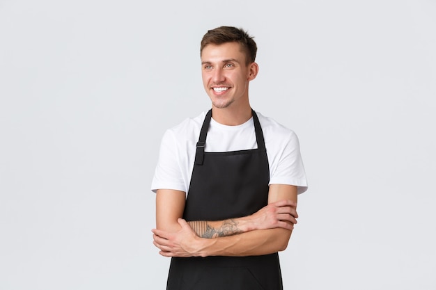 Photo gratuite propriétaires de petites entreprises, café et concept de personnel. beau mec blond joyeux, barista, travailleur à temps partiel, heureux dans le coin supérieur gauche avec un sourire satisfait, portant un tablier