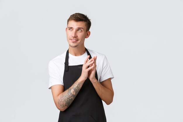 Propriétaires de petites entreprises, café et concept de personnel. Créatif et intelligent beau barista, serveur ou employé de café en tablier noir, doigts de clocher et sourire narquois, a une idée de génie, fond blanc