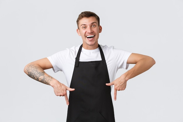 Propriétaires de petites entreprises, café et concept de personnel. Heureux barista amical, serveur en tablier noir pointant les doigts vers le bas, gars travaillant dans un café et montrant une promotion ou une annonce spéciale