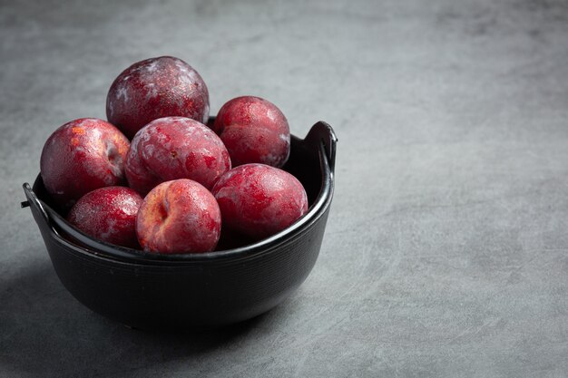 Prune rouge mis dans un bol noir sur sol sombre