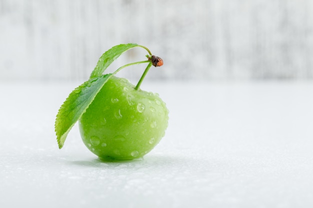 Photo gratuite prune verte avec des feuilles sur le mur grungy et blanc, vue latérale.