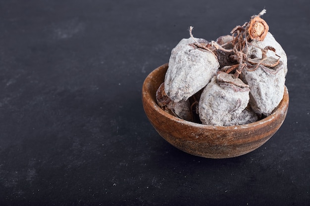 Prunes de dattes séchées dans une tasse en bois sur une surface grise.