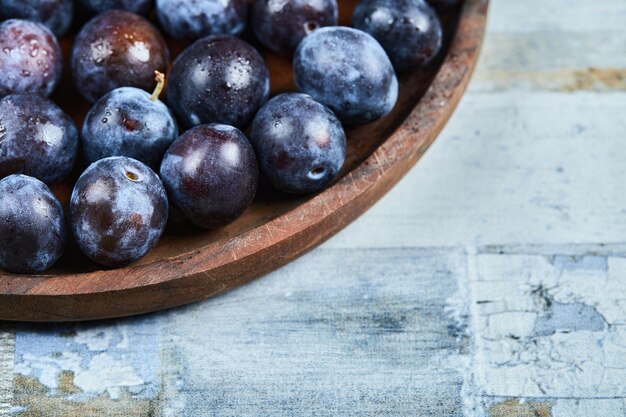 Prunes de jardin dans une assiette sur fond bleu. Photo de haute qualité