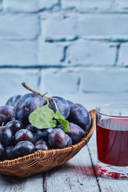 Prunes de jardin sur panier sur bleu avec un verre de jus.