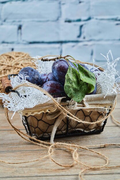 Prunes de jardin sur panier sur table en bois.