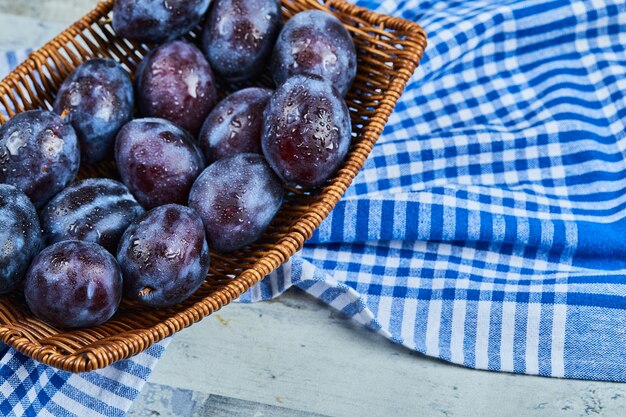 Prunes de jardin sur panier sur table en pierre avec nappe.