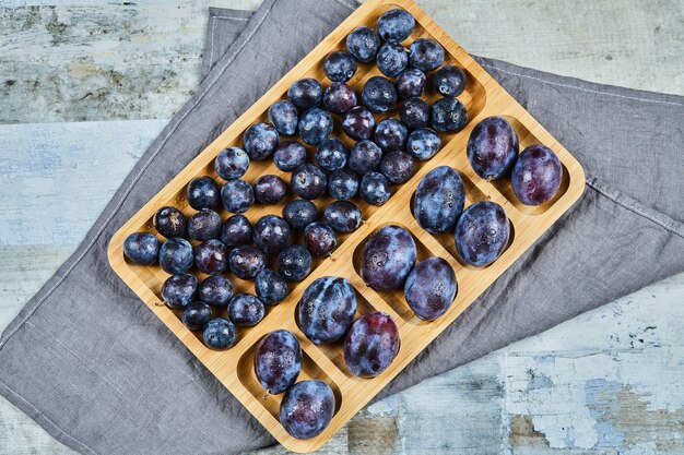 Prunes de jardin sur plateau en bois avec nappe grise.