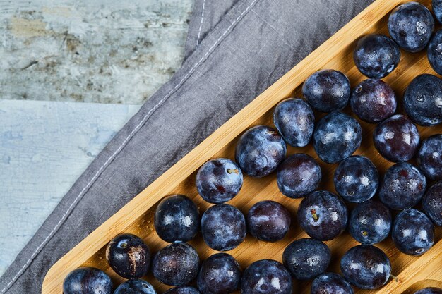 Prunes de jardin sur plateau en bois avec nappe grise.