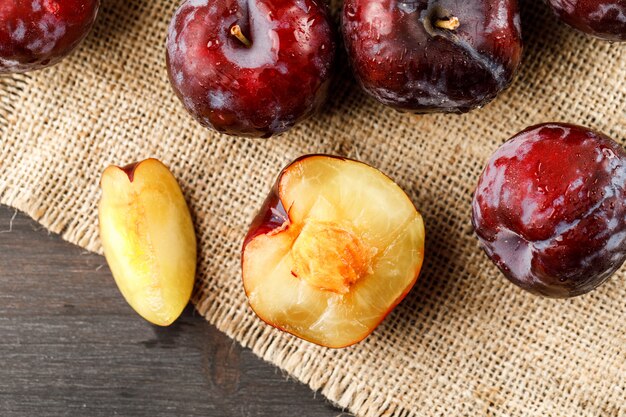 Prunes rouges sur fond gris et morceau de sac, à plat.