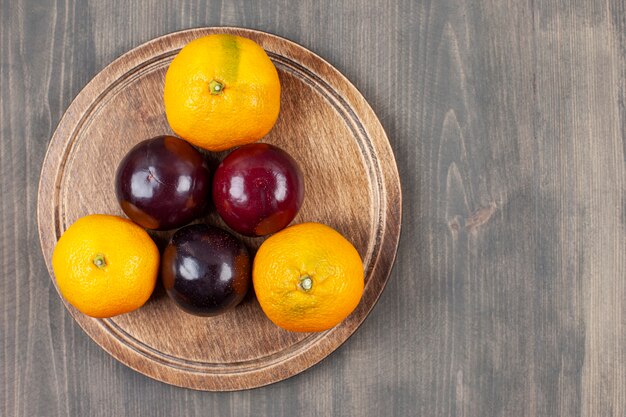 Prunes savoureuses avec de délicieuses mandarines sur une assiette en bois. Photo de haute qualité