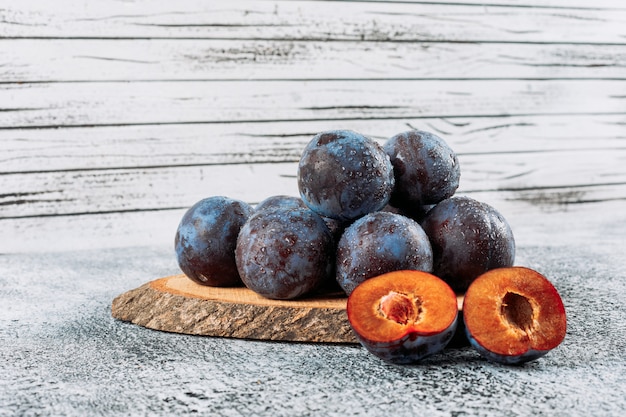 Prunes en tranches fraîches dans une planche de bois sur fond de stuc gris, vue latérale.