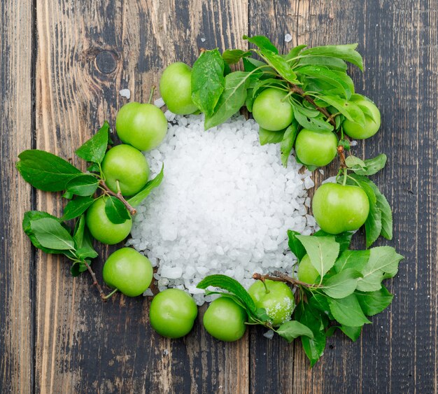 Prunes vertes avec cristaux de sel, feuilles sur mur en bois, pose à plat.