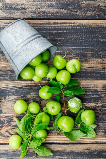 Photo gratuite prunes vertes éparses avec des feuilles, sel d'un mini seau sur mur en bois, vue de dessus.