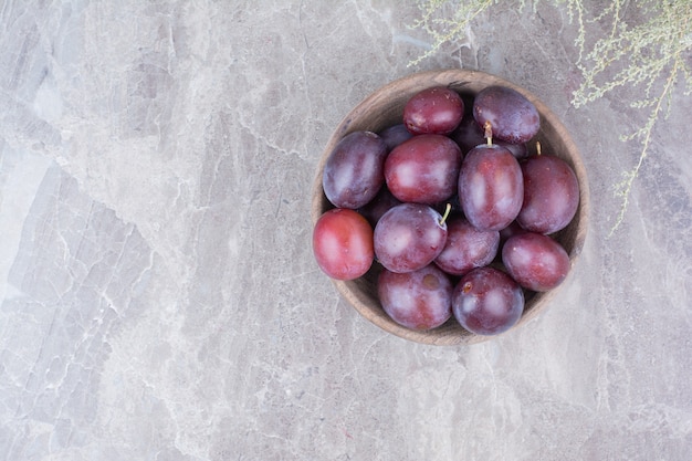 Prunes violettes dans un bol en bois sur fond de pierre.