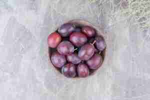 Photo gratuite prunes violettes dans un bol en bois sur fond de pierre.