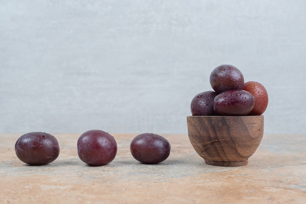 Prunes violettes mûres dans un bol sur fond de marbre.