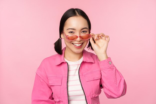 Publicité de lunettes Une fille asiatique moderne et élégante touche des lunettes de soleil porte des poses roses sur fond de studio Espace de copie