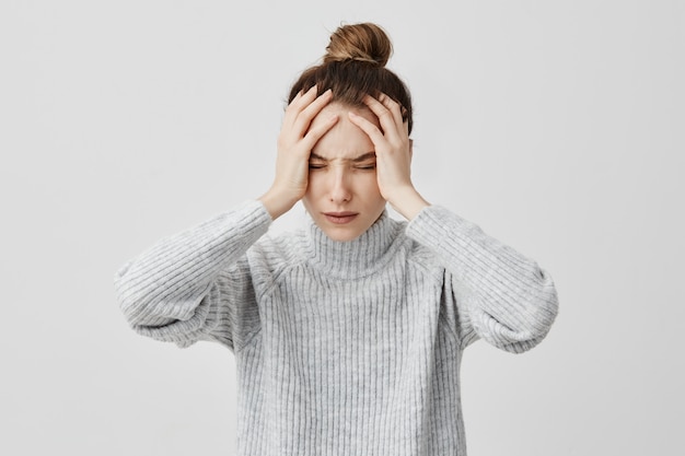 Épuisée jeune femme touchant la tête, les yeux fermés. Travailleuse d'échange souffrant de maux de tête insupportables. Concept de santé