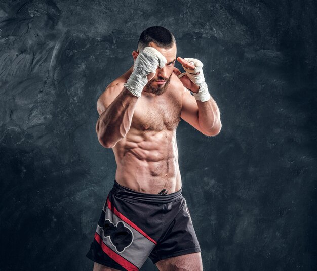 Un puissant combattant musclé montre son coup de poing tout en posant pour un photographe dans un studio photo sombre.