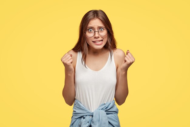 Puissante jeune brune avec des lunettes posant contre le mur jaune