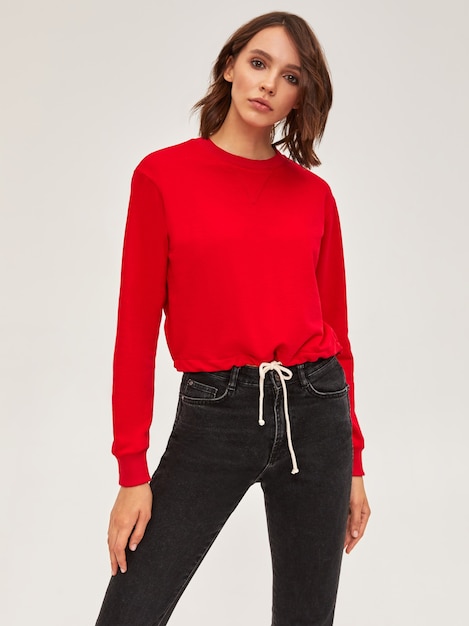 Photo gratuite pull rouge et jean skinny noir sur fille mince moderne aux cheveux courts brune. debout en studio sur fond blanc.