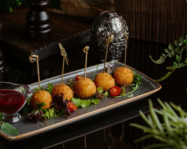 Purée de pommes de terre et boulettes de fromage grillées et servies avec une salade verte dans une assiette en granit carrée