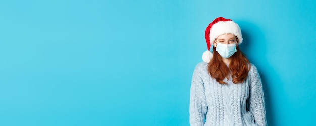 Photo gratuite quarantaine de noël et concept covid modèle féminin rousse effronté en masque facial et bonnet de noel winkin