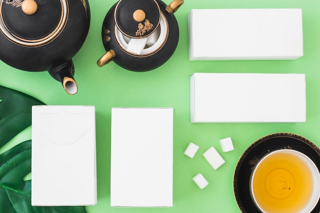 Quatre boîtes blanches avec des tisanes et des cubes de sucre sur fond vert