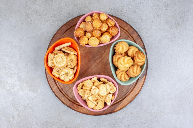 Quatre bols de biscuits et chips de biscuits sur planche de bois sur une surface en marbre.