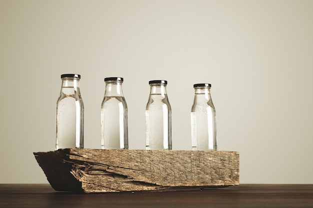 Quatre bouteilles en verre transparent clair avec des bouchons noirs remplis d'eau potable pure présentée sur la brique en bois, isolé sur blanc