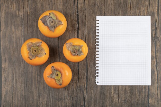 Quatre fruits mûrs de kaki et cahier vide sur la surface en bois