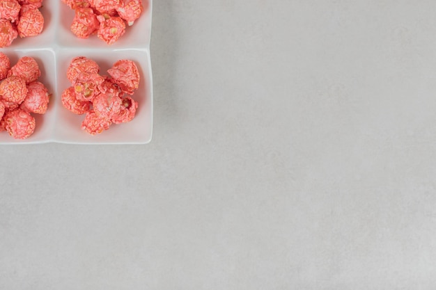 Quatre portions de maïs soufflé enrobé de bonbons dans un plateau de collations sur une table en marbre.