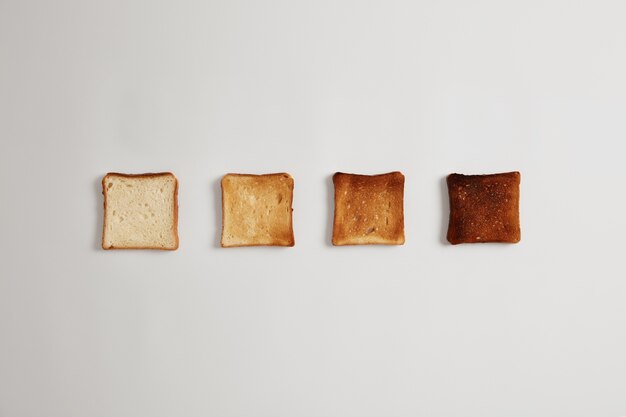 Quatre tranches de pain de grillé à brûlé préparées dans un grille-pain disposées en ligne contre une surface blanche. Ensemble de morceaux de pain grillé pour faire un délicieux sandwich croustillant. Délicieux petit-déjeuner, cuisine