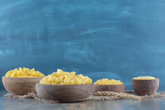 Quatre types de pâtes dans des bols, sur la surface en marbre.